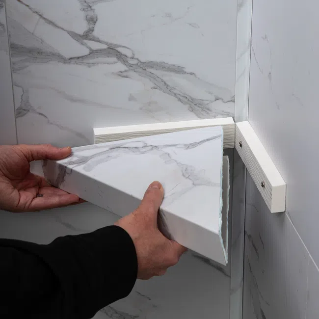 Person installing a triangular marble shelf on white marble wall with white wooden supports