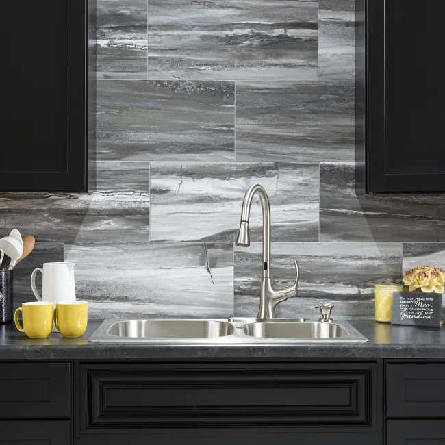 Modern kitchen sink with stainless steel faucet, gray marble backsplash, black cabinets, and yellow mugs on countertop.