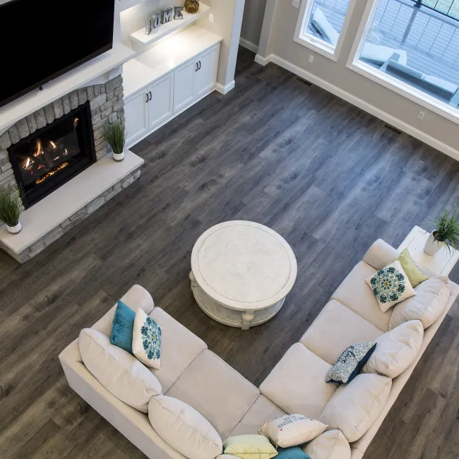 Top view of a modern living room with gray wood floors, beige sectional sofa, round coffee table, and stone fireplace.
