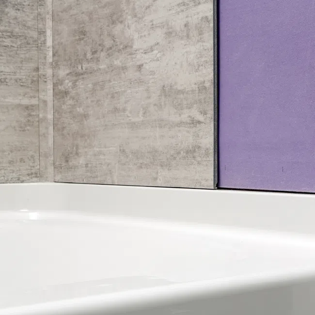Close-up of a white bathtub with textured gray and purple bathroom wall tiles behind it.