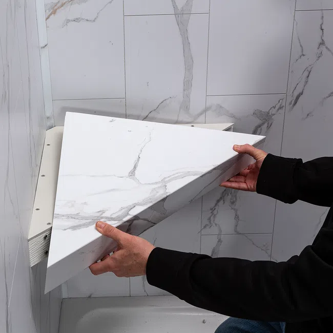 Person installing a removable white marble patterned corner panel in a tiled bathroom corner.