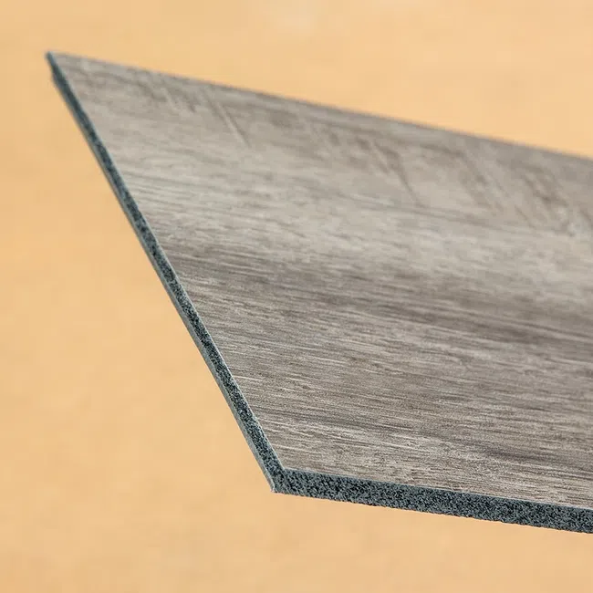 Close-up of a gray wood-textured vinyl plank with a beveled edge against a beige background