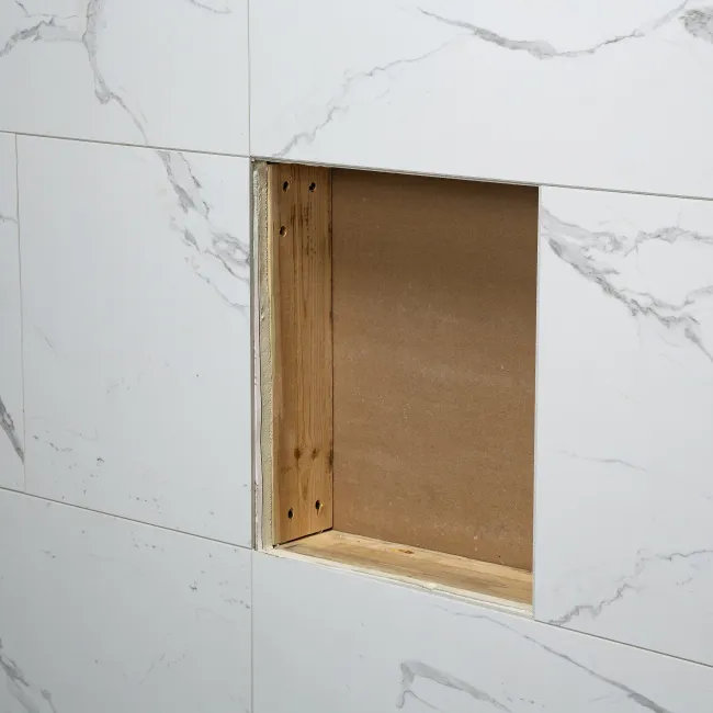 White marble tiled wall with a square cutout revealing wooden framing behind the tile surface.