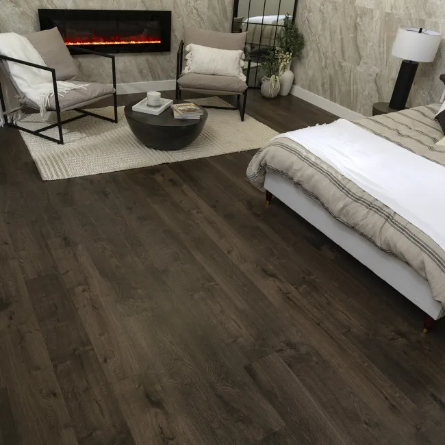 Cozy bedroom with dark wood floor, modern fireplace, neutral bedding, and sitting area with armchairs and rug.