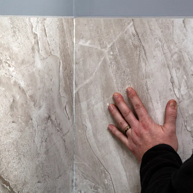 Close-up of a hand touching large beige marble tiles with natural veining and texture.