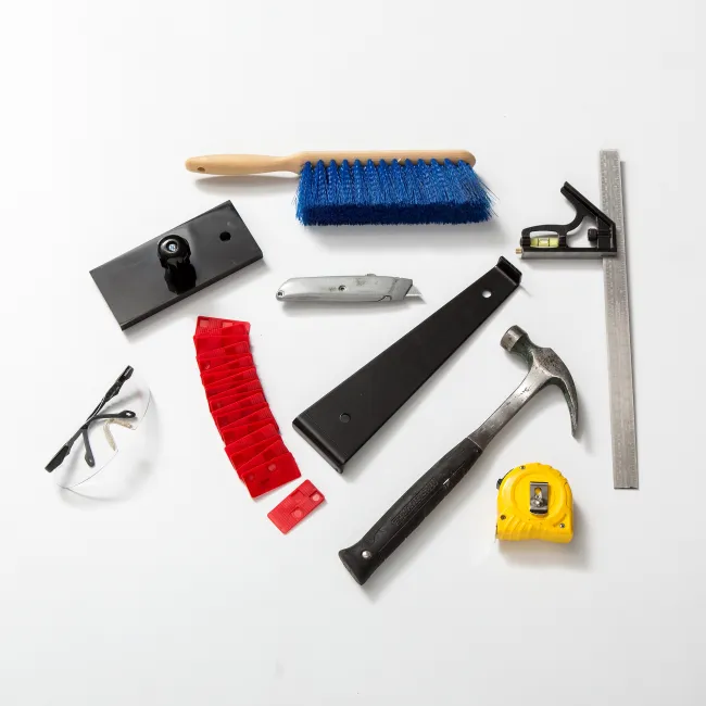 Collection of various hand tools including hammer, brush, measuring tape, utility knife, safety glasses on white background.