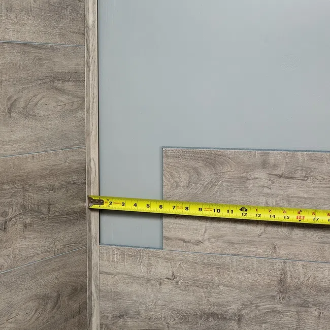 Worker measuring wood paneling with a yellow tape measure against a gray wall during installation.