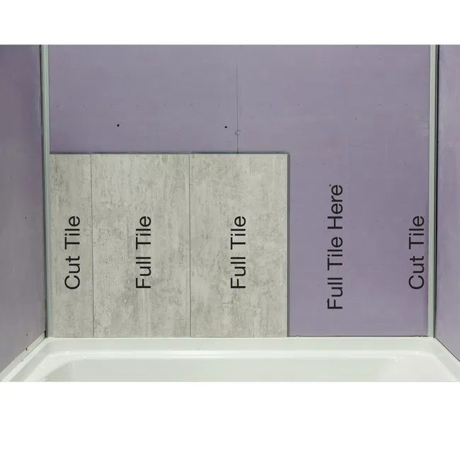 Wall with labeled areas for cut and full tiles partially installed above a bathtub in a bathroom.