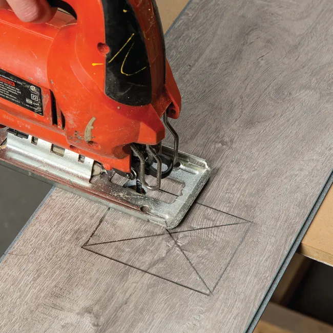 Red jigsaw cutting a rectangular hole outlined on a wooden board during a carpentry project.