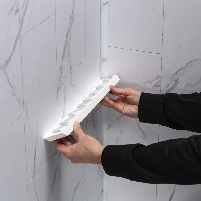 Hands installing a white corner tile shelf on a marble-patterned tiled wall in a bathroom or kitchen corner.