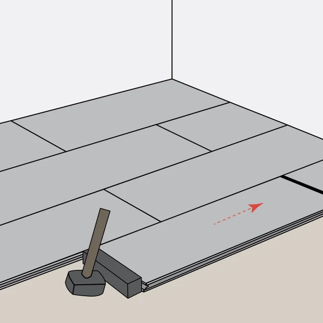 Installing gray wooden floor planks with a rubber mallet and tapping block in a staggered pattern in a room corner.
