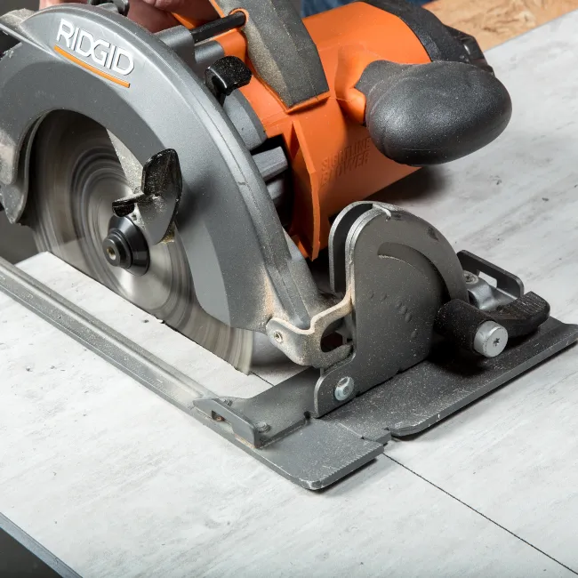 Close-up of a Ridgid circular saw cutting through a wooden board controlled by a person's hand.
