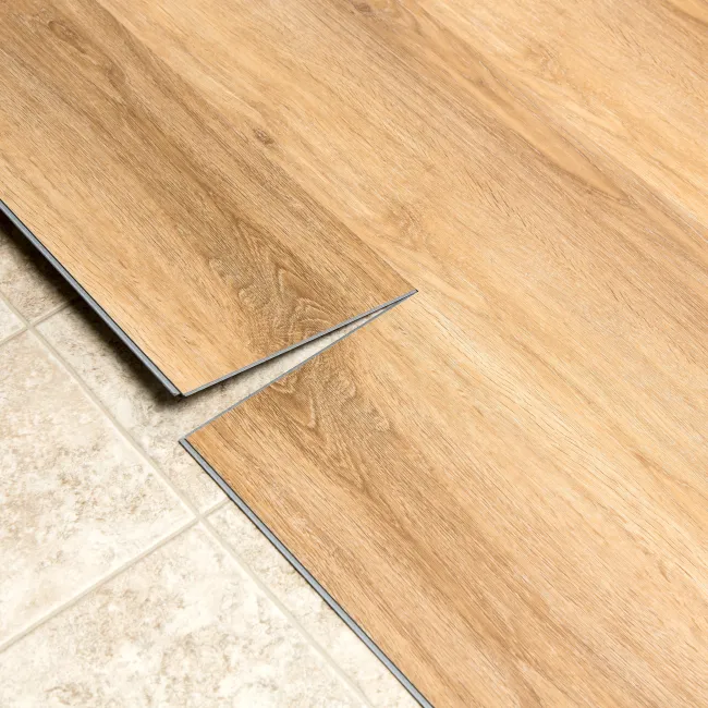 Installation of wood-look vinyl plank flooring next to beige ceramic tile on the floor.