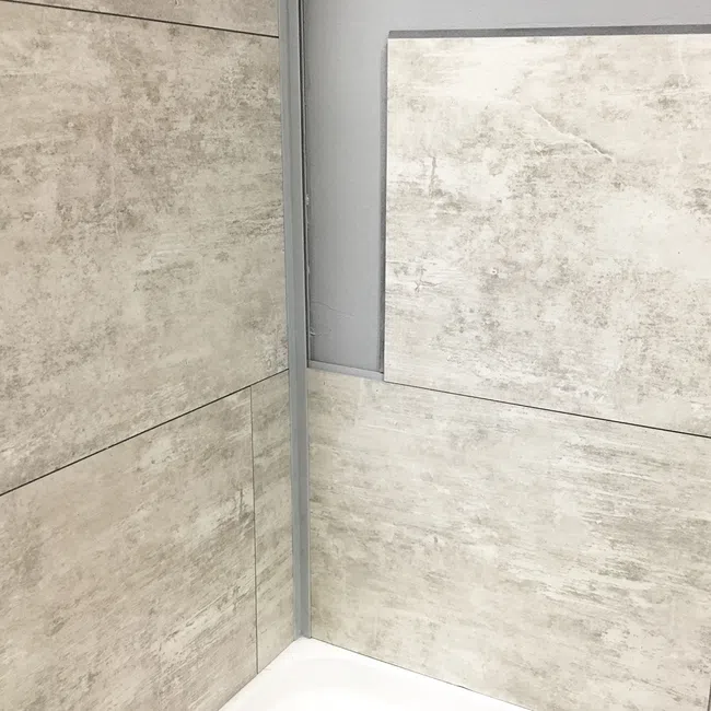 Close-up of beige textured wall tiles in a corner above a white bathtub with gray grout lines.