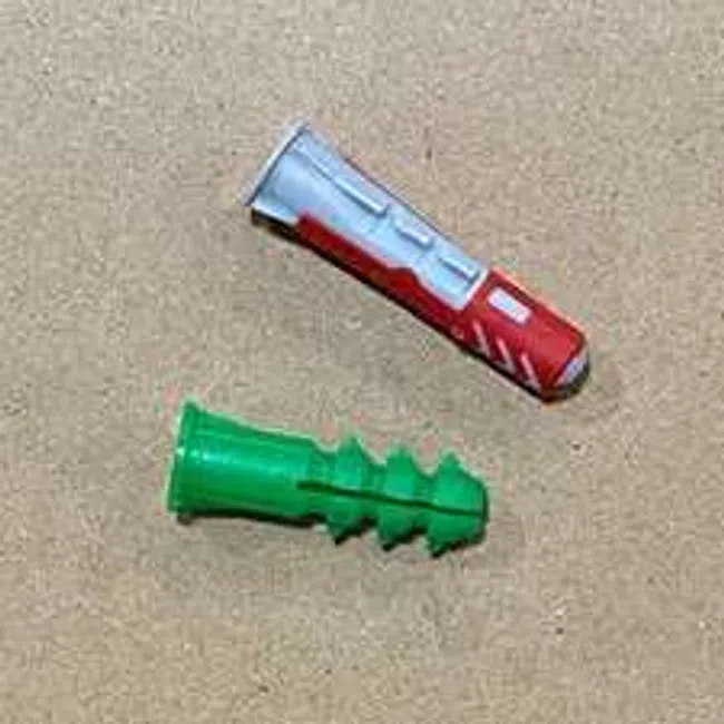 Two different colored plastic wall anchors, one green and one gray with red, on a beige surface.