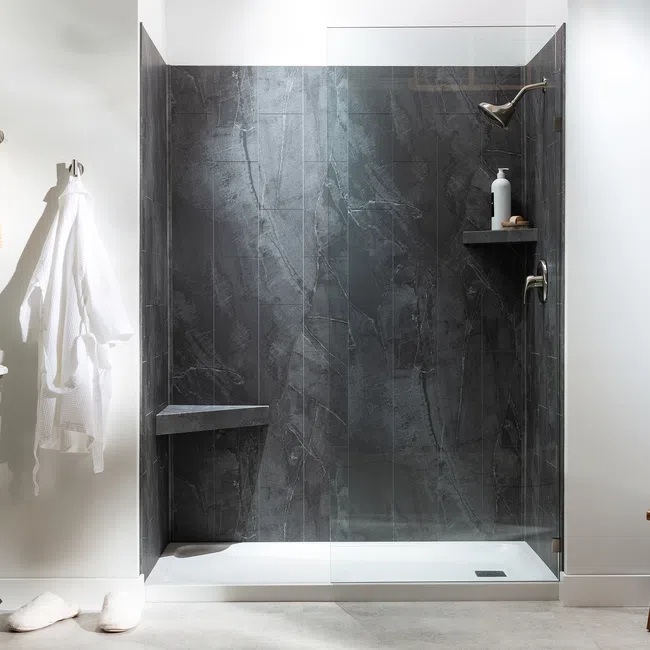 Modern bathroom with dark stone walk-in shower, wooden vanity, white walls, and wooden stool with toiletries.