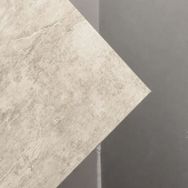 Beige textured tile placed diagonally on dark gray smooth surface showing contrast of materials.