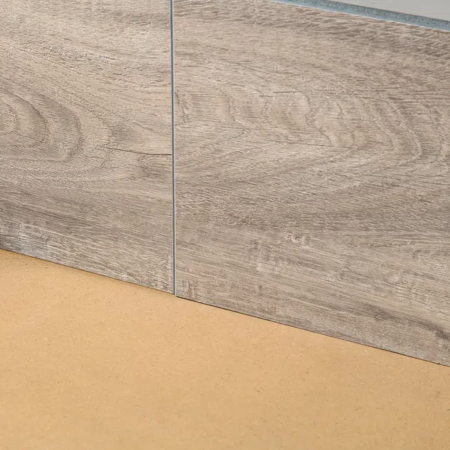 Close-up of two light brown wood-textured tiles placed on a beige surface with clear grout lines.