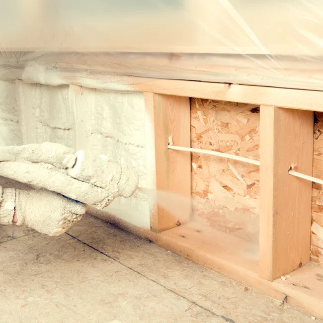 Worker spraying foam insulation into wall cavity during home construction or renovation.