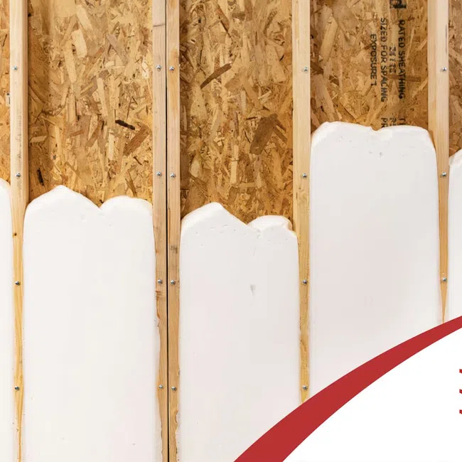 White spray foam insulation applied between wooden wall studs on plywood sheathing for energy efficiency.