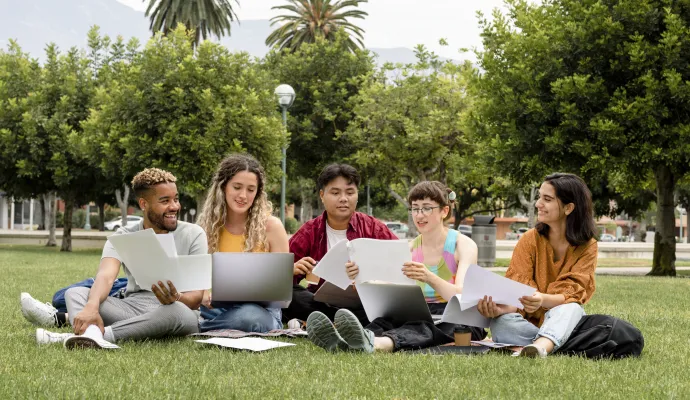 a group of people sitting on the grass with laptops