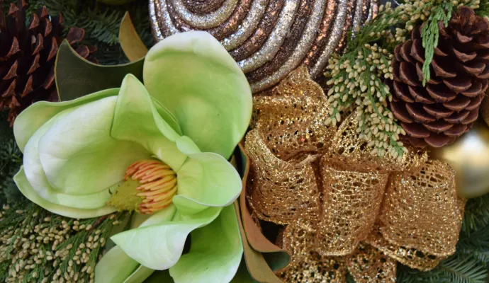Close-up of a festive holiday arrangement with a green flower, pinecone, gold ribbon, and glittery ornaments.