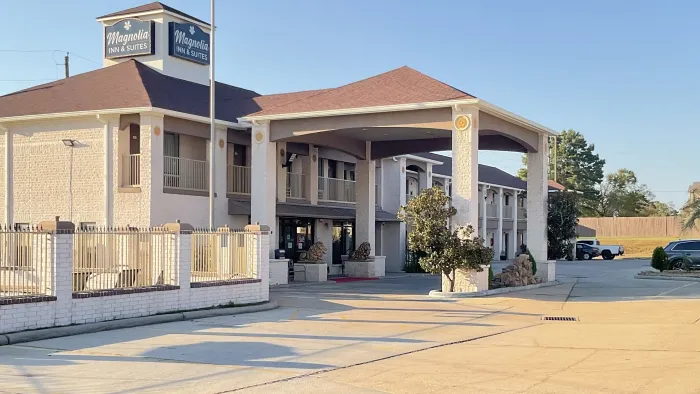 Exterior view of Magnolia Inn & Suites with covered entrance, parking area, and clear blue sky on a sunny day.