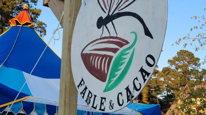 Sign for Fable & Cacao handmade chocolate treats displayed on wooden post near blue tent outdoors.
