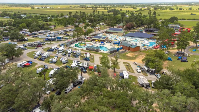 Aerial view of a large RV campground with swimming pools, water slides, and surrounding green fields under clear sky.