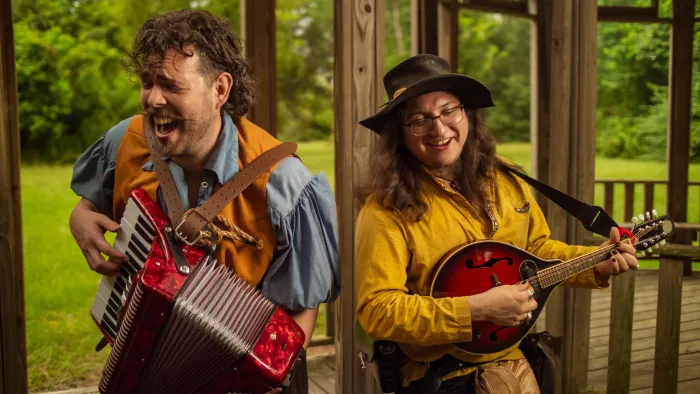 Two joyful musicians playing accordion and mandolin on a wooden porch with greenery outside