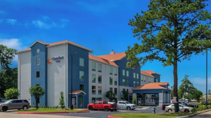 Comfort Inn hotel building with blue and white facade, red truck in parking lot, and clear blue sky above