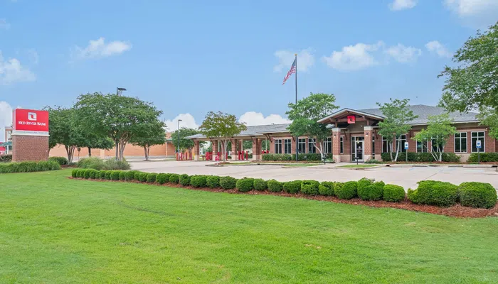 Red River Bank building with American flag, green lawn, and clear blue sky on a sunny day