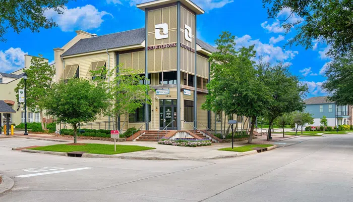 Modern Red River Bank building surrounded by trees under a bright blue sky on a street corner.