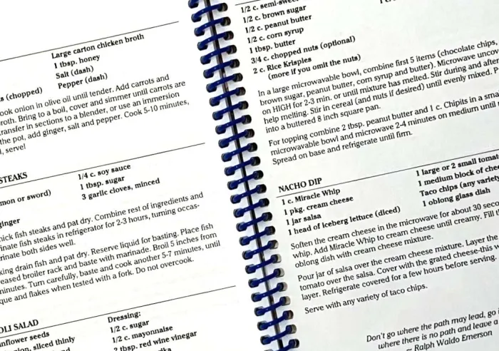 Open spiral-bound cookbook displaying detailed recipes including ingredients and instructions for various dishes