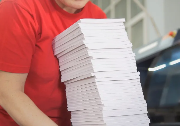 A printing plant worker holding a large stack of Perfect Bound books