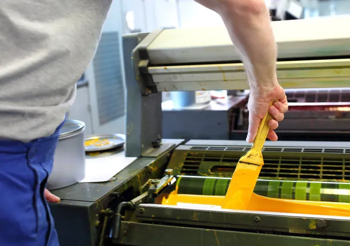 Man adding yellow ink to an offset printing press