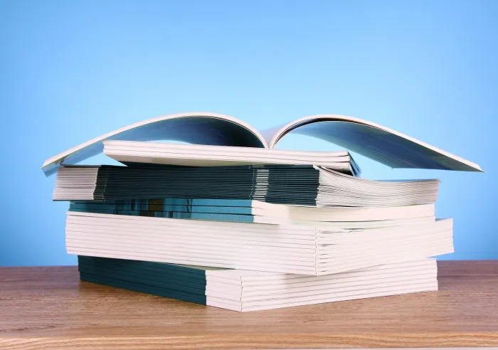 A stack of miscellaneous booklets on a wooden surface against a blue background
