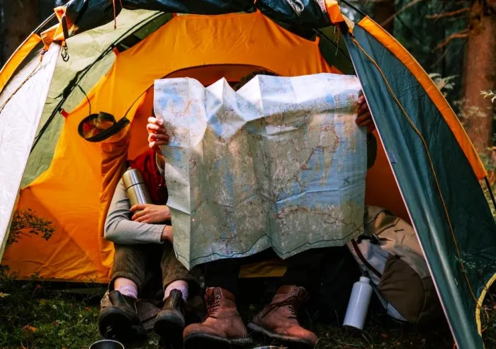 Two campers sitting in front of a tent surveying a large printed map