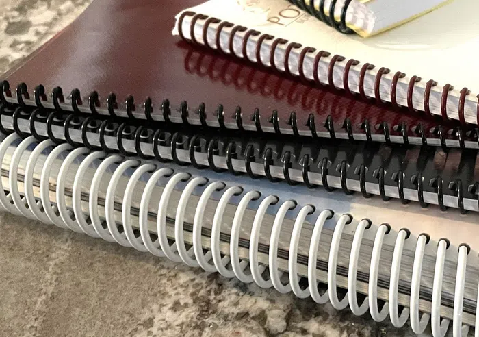 Close-up of stacked spiral-bound books with black, white, and maroon covers.