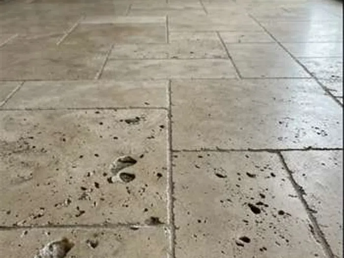 Close-up view of worn and pitted travertine stone flooring with visible surface damage and discoloration.