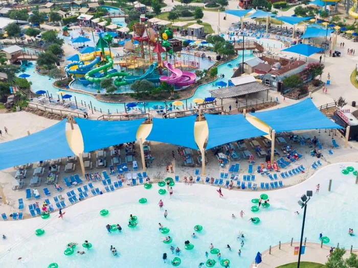 Group of kids riding a large blue inflatable raft down a colorful water slide on a sunny day.