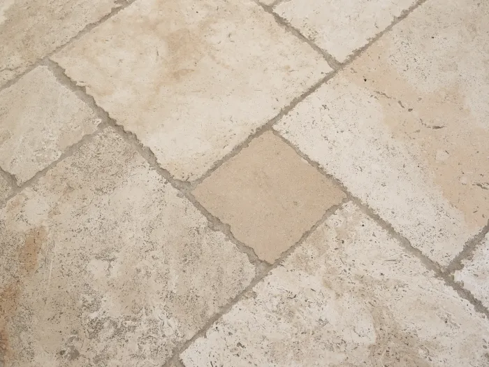 a close-up of a stone tile floor with dirty flecks and dark grout lines