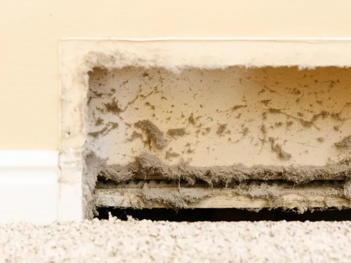 Inside look of a cold air register with its cover off, exposing lines of dirt and dust sticking to it