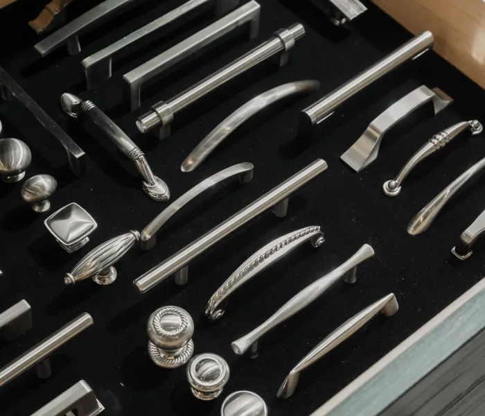 Drawer displaying a variety of brushed nickel cabinet handles and cabinet knobs arranged on black felt.