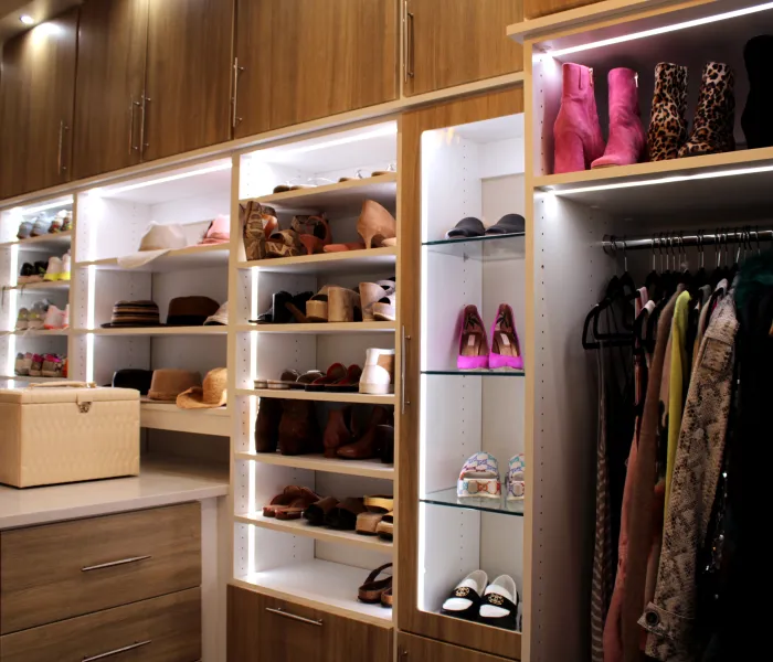Walk in closet with glass shelves, white shelves, an island, hanging clothes, shoes, hats and accent lighting on each shelf