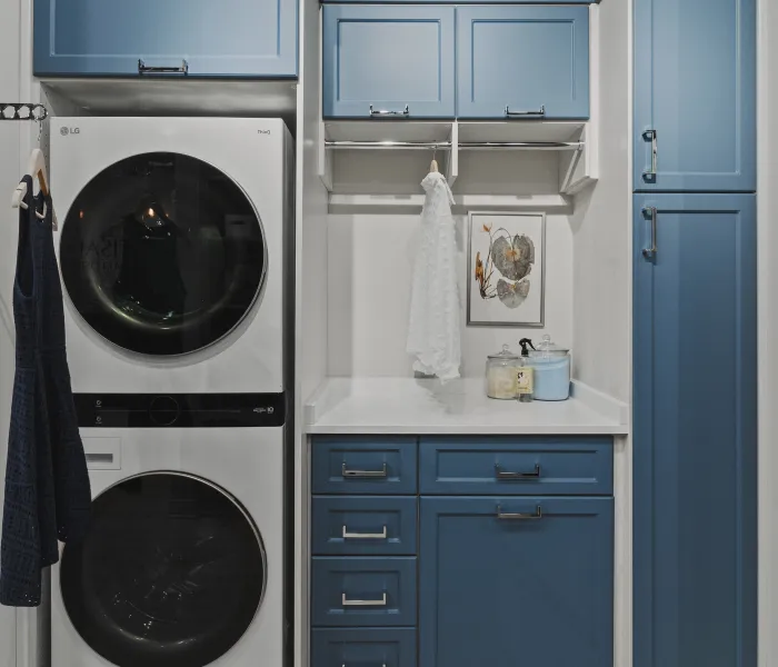 Laundry room with stacked white LG washer and dryer, a white marble counter, blue cabinets, clothing rod and hanging clothes
