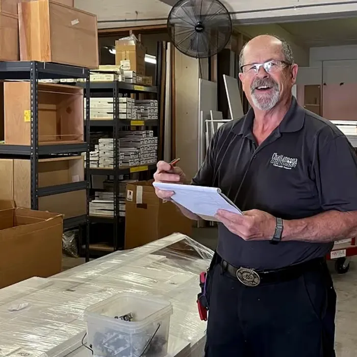 Smiling warehouse worker holding clipboard and pen in storage room with shelves, boxes, and tools around him