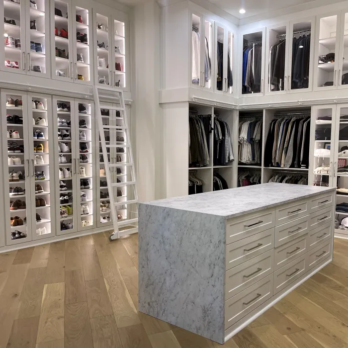 a white full room closet with a white quartz countertop island and a white shoe wall with a white lilbrary ladder