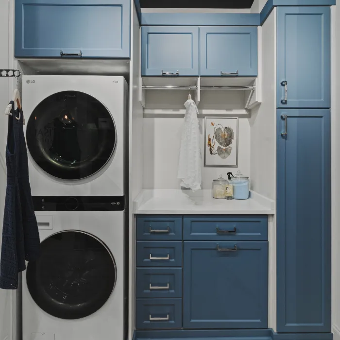 Laundry room with stacked washer and dryer, blue cabinets, white countertop, hanging rod for clothing, laundry supplies