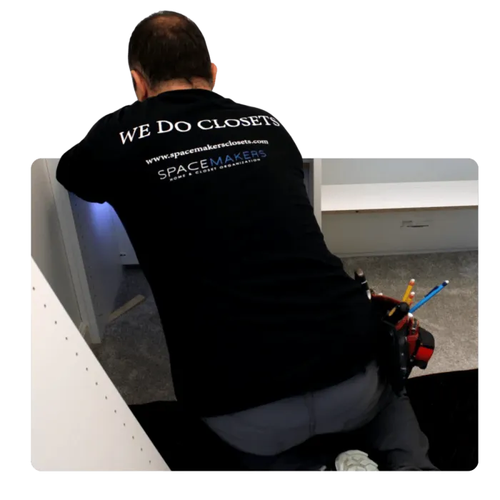Technician installing custom white closet shelving wearing a black Spacemakers shirt with tools at his waist.